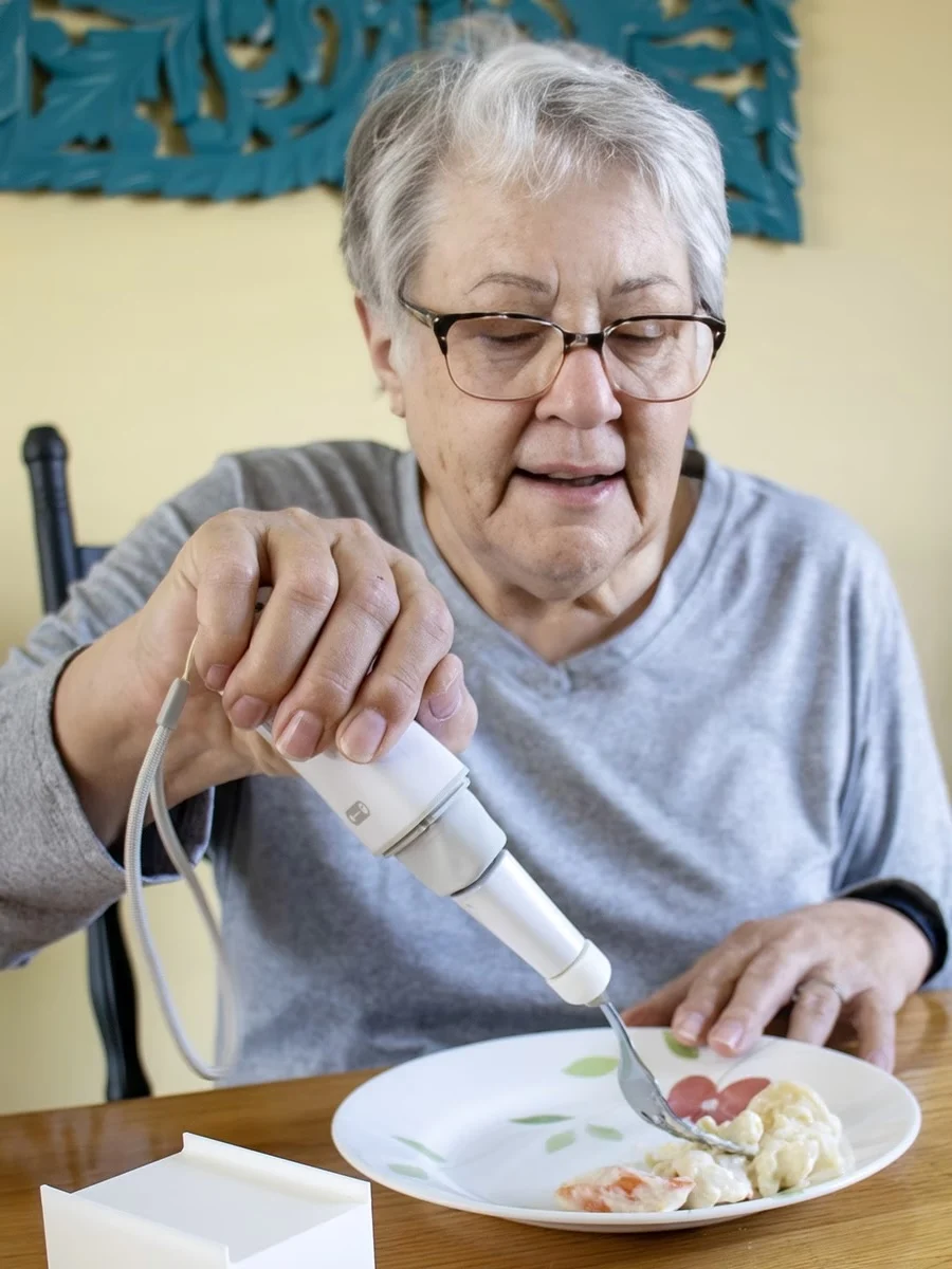 Person with adapted spoon to eat from a white plate on a table